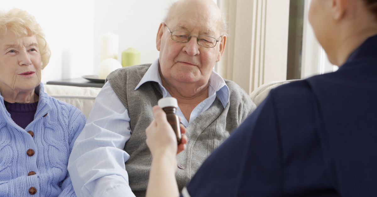 Senior Couple Meeting With A Nurse To Discuss Their Medications.