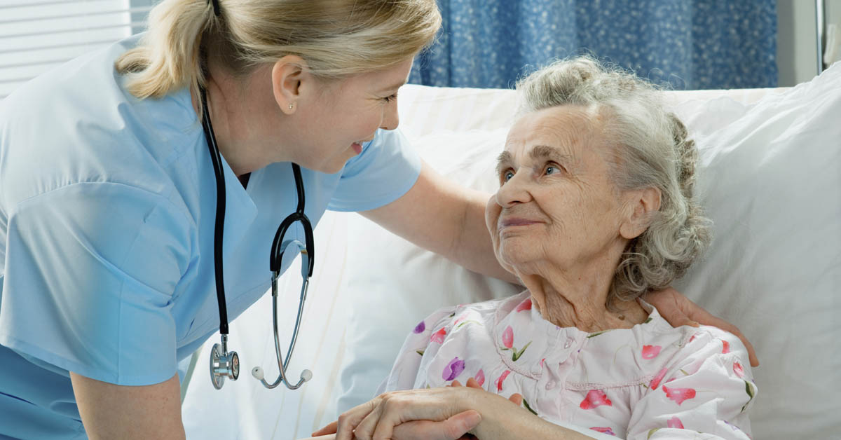 Nurse Comforting An Elderly Lady In Bed.